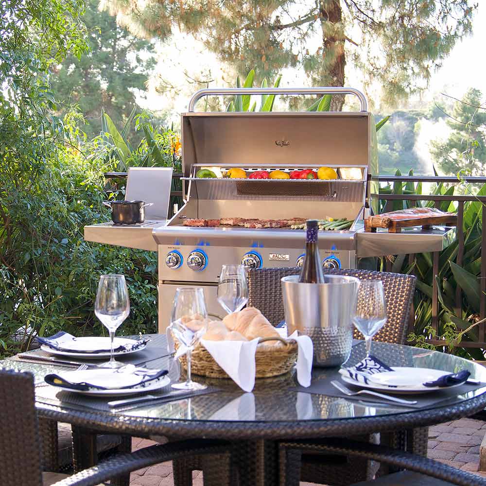 Outdoor gas grill with open hood and front burners on a patio table