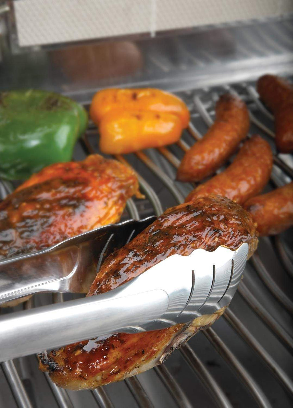 Stainless steel locking tongs holding grilled sausages on a barbecue