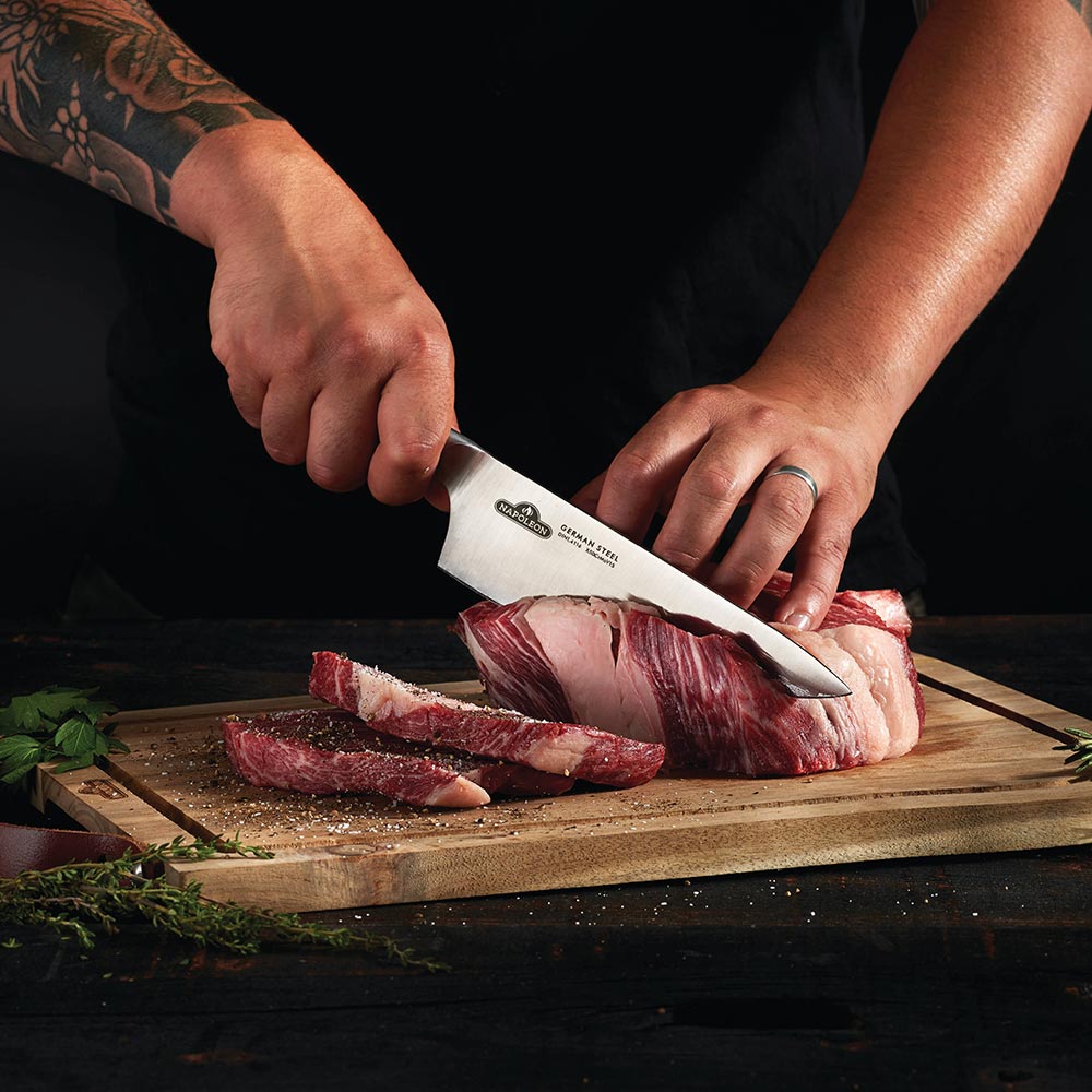 Chef's knife slicing meat on a wooden cutting board, held in two hands