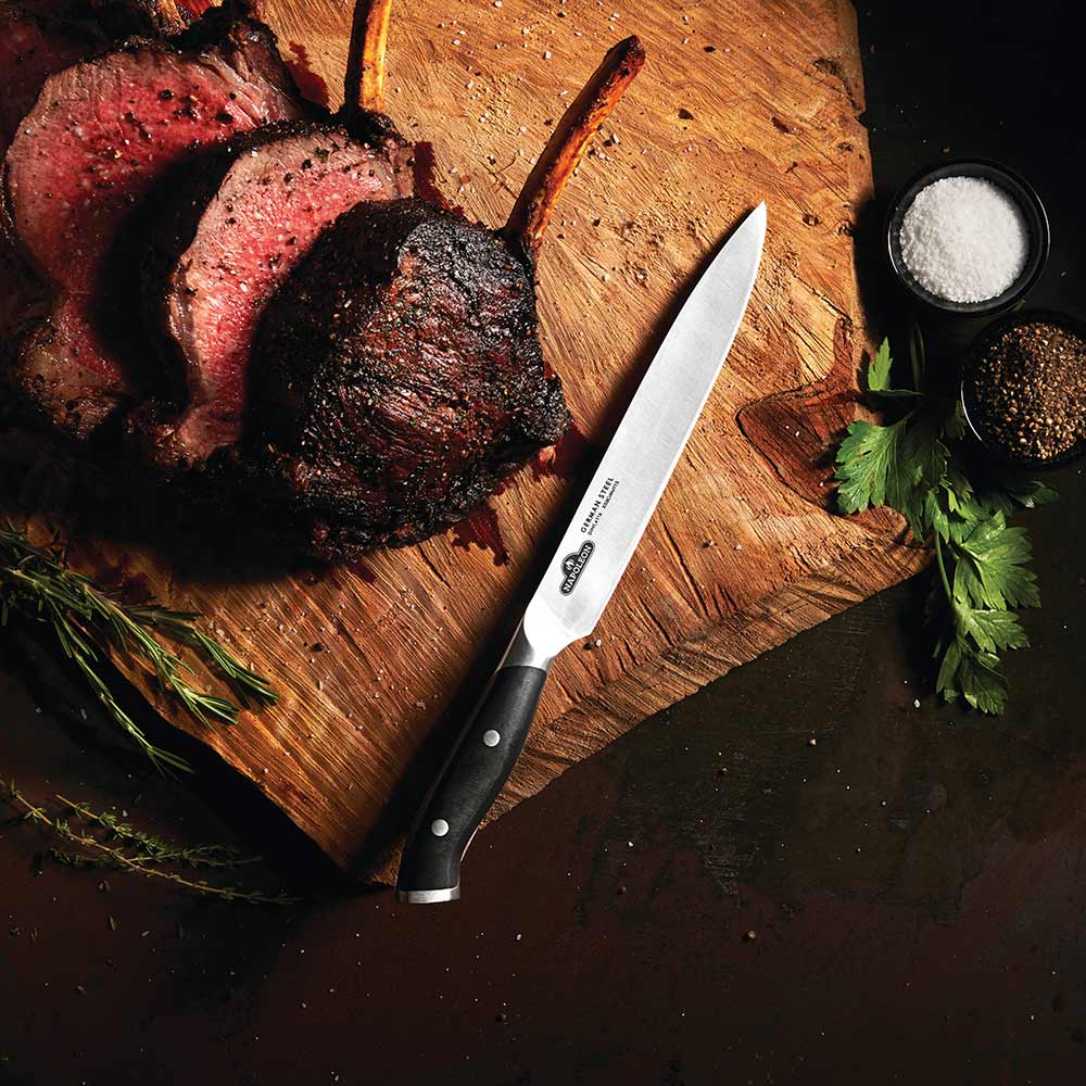 Carving knife angled on board, stainless steel blade and black handle with rivets