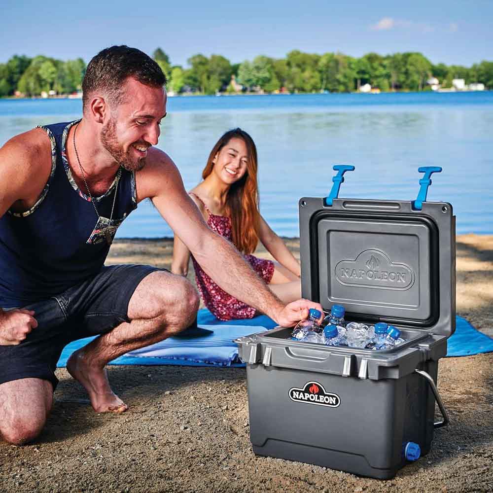 Gray cooler chest open with ice and bottles, Napoleon logo, beach setup