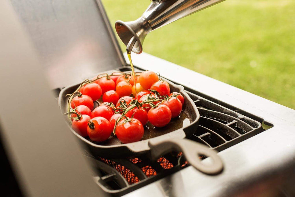 Cast iron sizzle platter skillet holding whole tomatoes on an outdoor grill