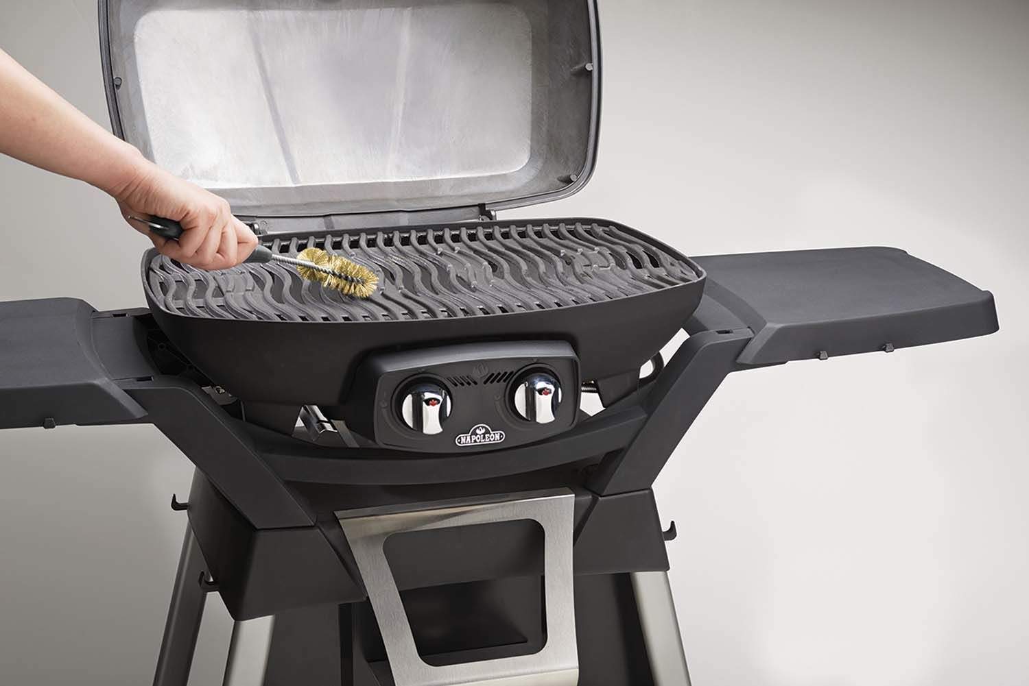 Grill brush with bottle opener scrubbing grill grates, tan bristles on black handle