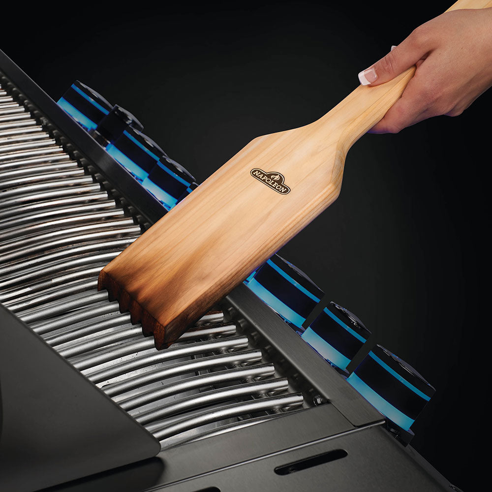 Cedar wood grill grid scraper held against metal grates