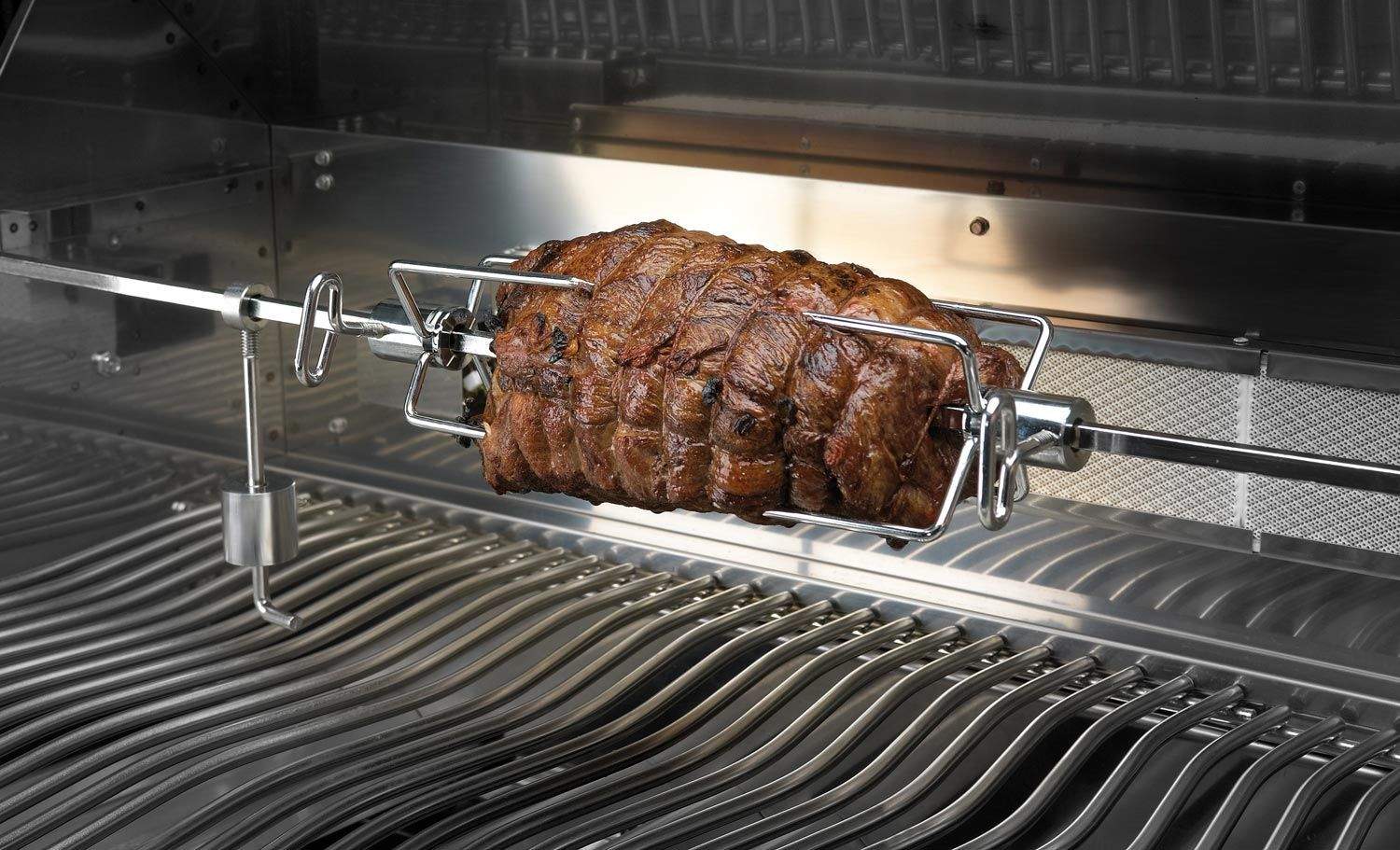 Rotisserie spit holding a roast chicken inside the grill, over stainless grates.