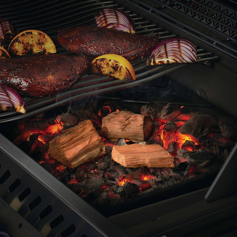 Burning apple wood chunks on grill grate with charred meat beside them