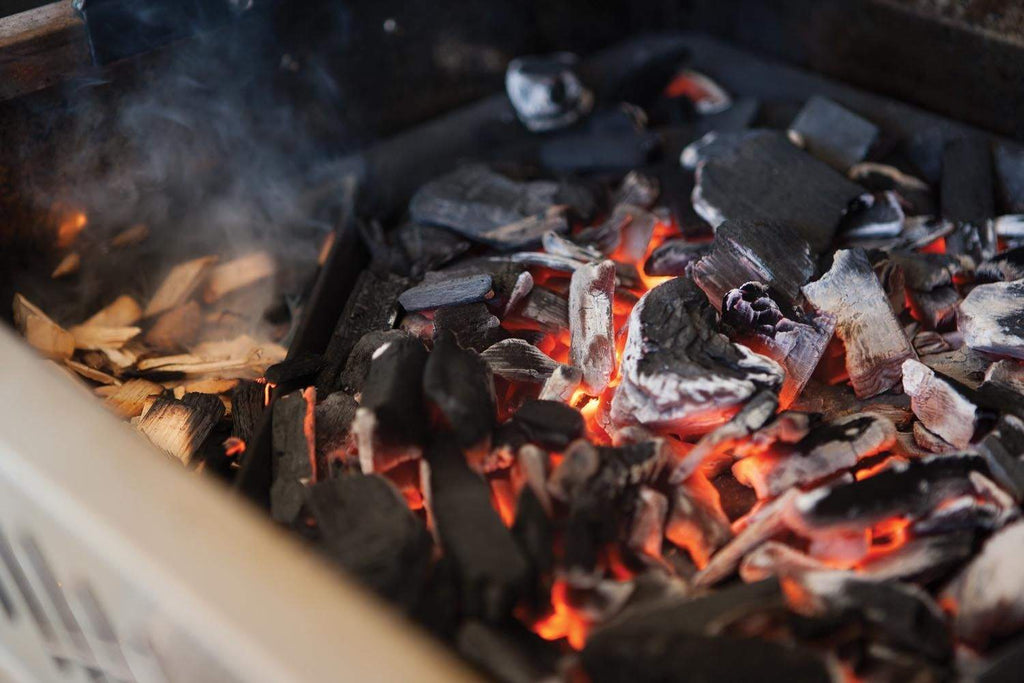 Burning charcoal in a smoker tray, glowing red coals and orange flames