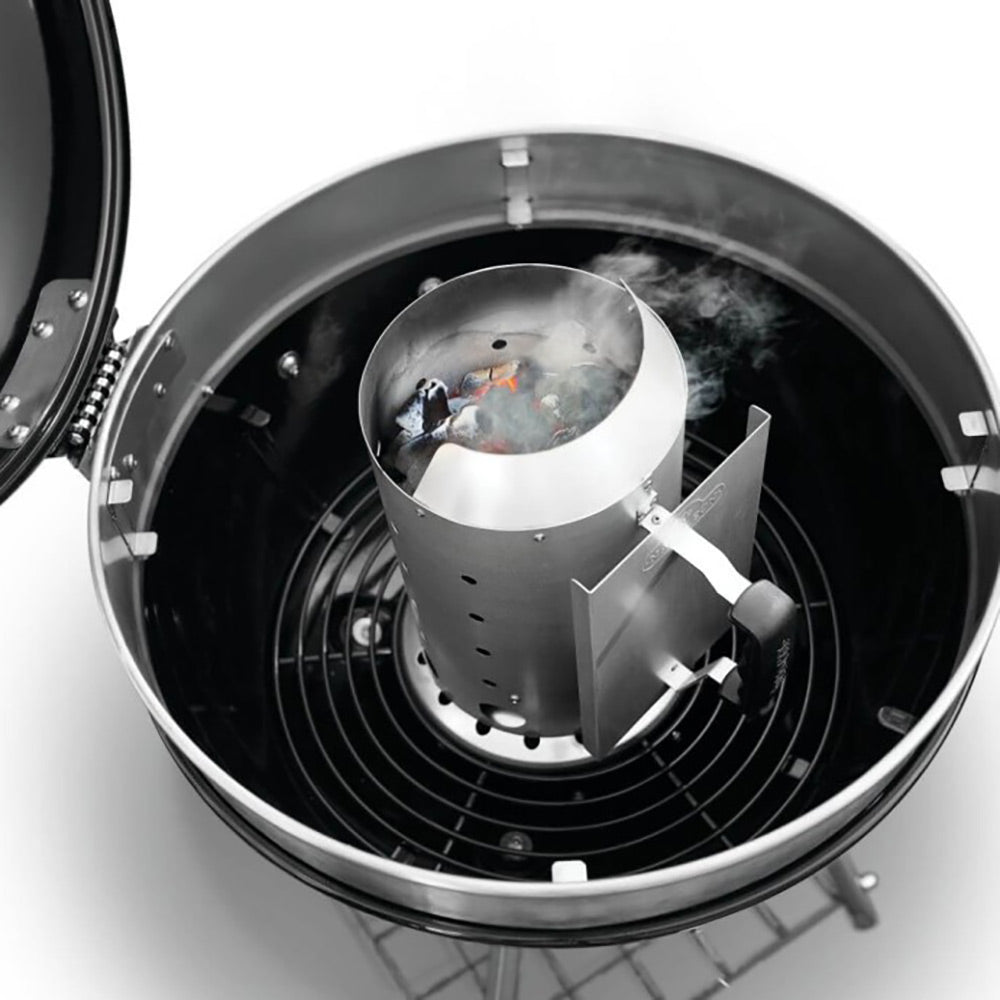 Charcoal chimney starter inside a grill with glowing coals and light smoke