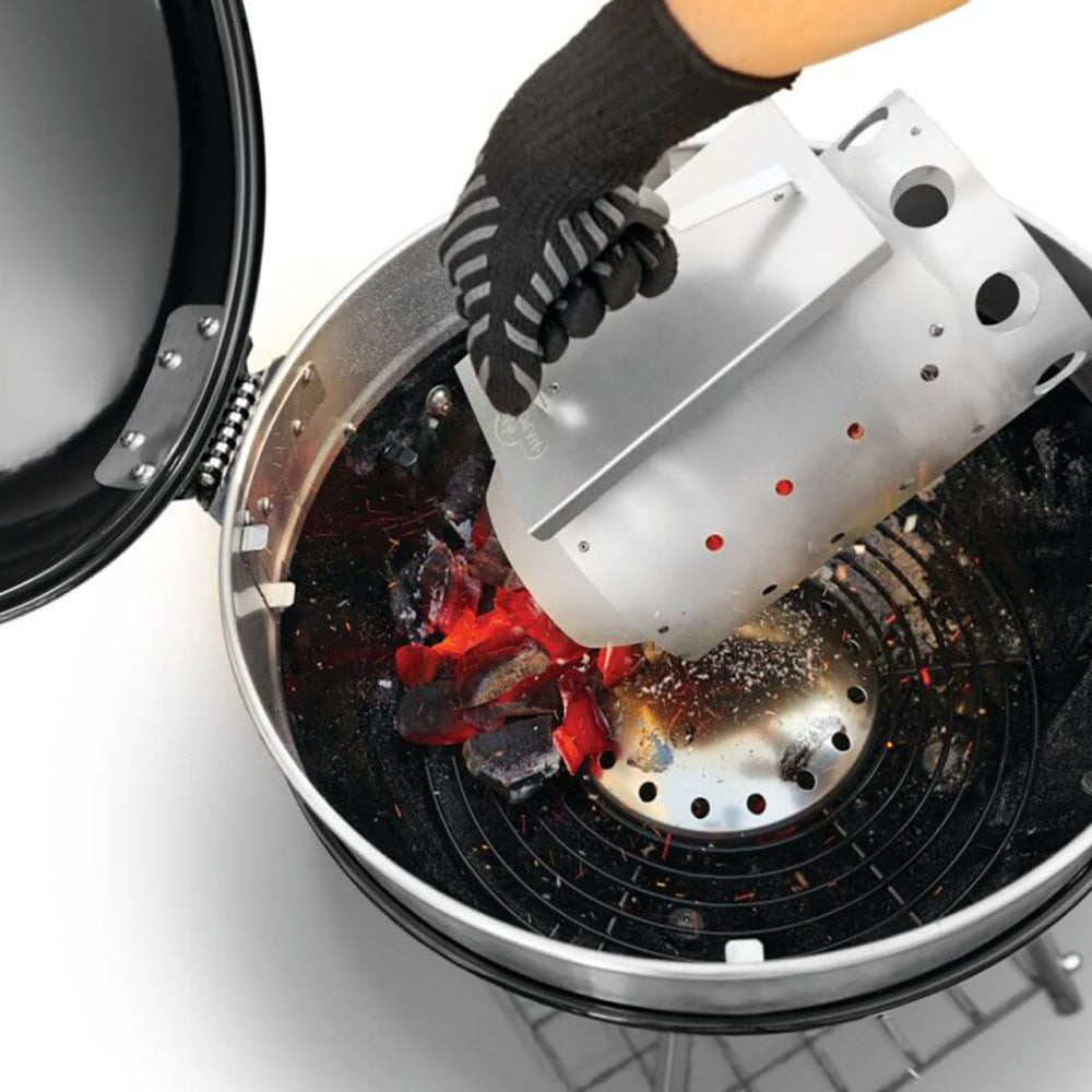 Charcoal starter chimney tipping into a grill with glowing coals and flames