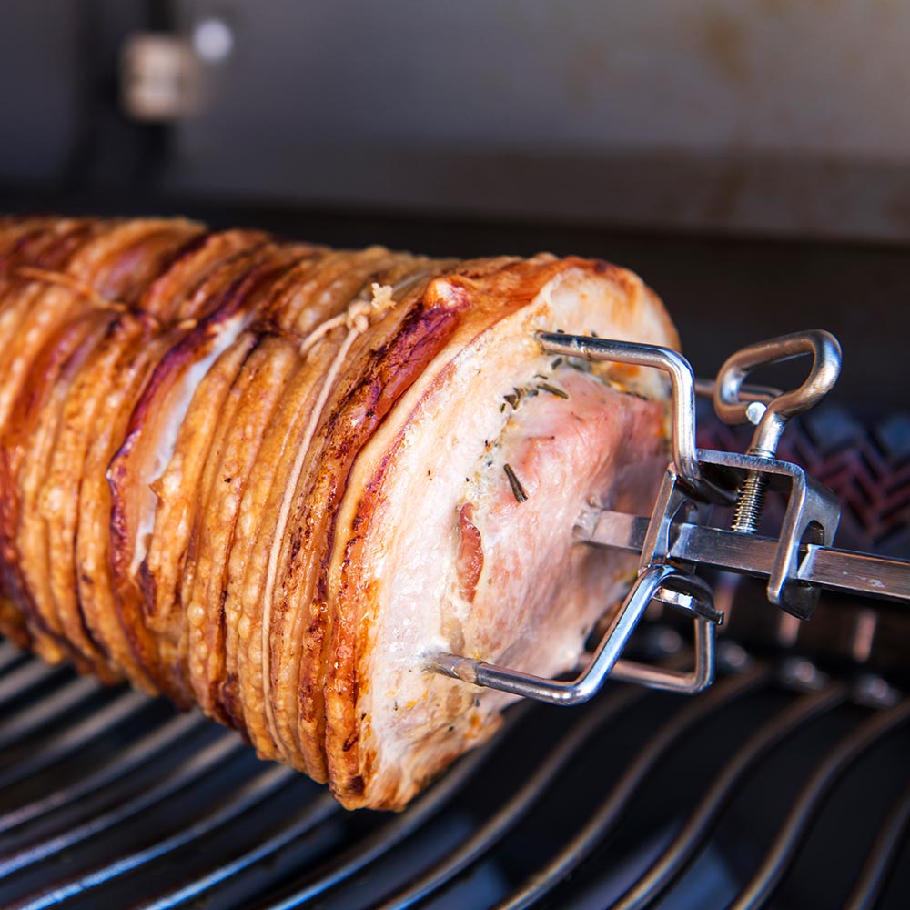 Rotisserie spit with forks holding roasted meat on grill grates
