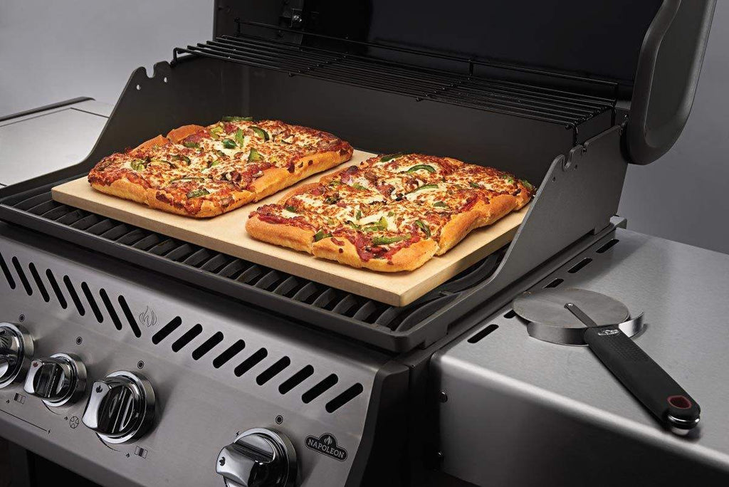 Rectangular baking stone on grill with topped pizza on it