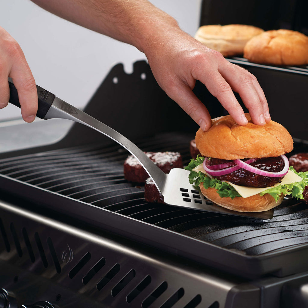 Grill tool set spatula in hand lifting a burger on a hot grill