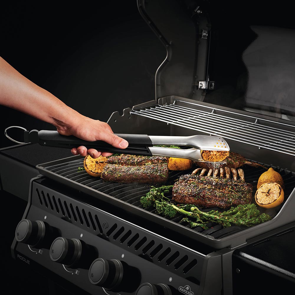 Stainless-steel spatula and turner with black handles placing food on a grill rack