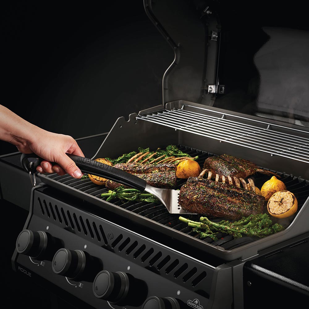 Grilling tools with black handles moving steaks and vegetables on a hot grill grate