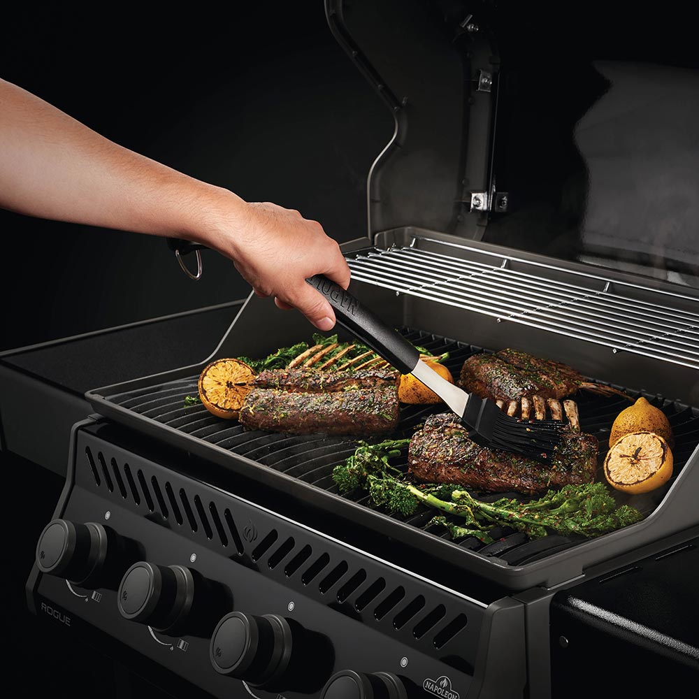 Hands using a black-handled spatula to turn grilled meat on a stainless grill rack