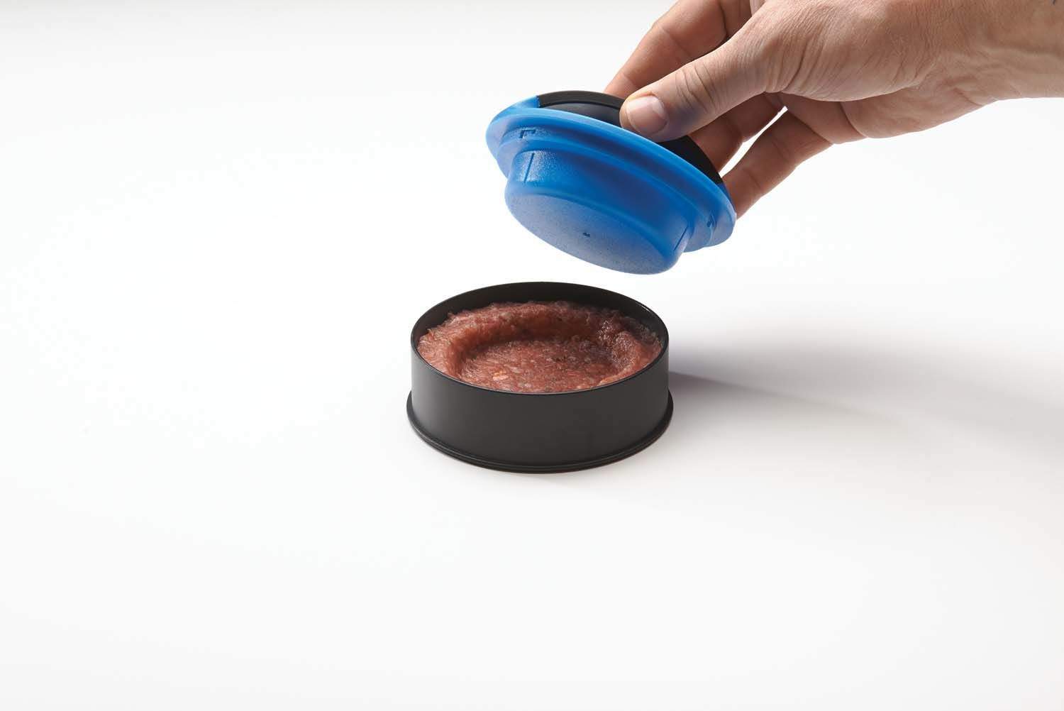 Hand pressing blue lid onto burger patty in black round mold