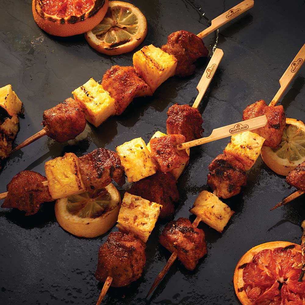 Bamboo skewers holding grilled meat cubes and sausage rounds