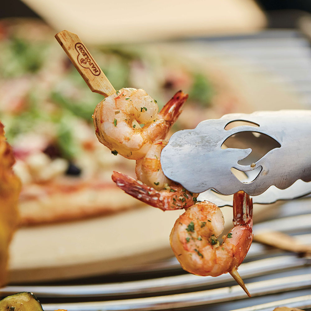 Bamboo skewer holding shrimp with herbs beside a metal fork