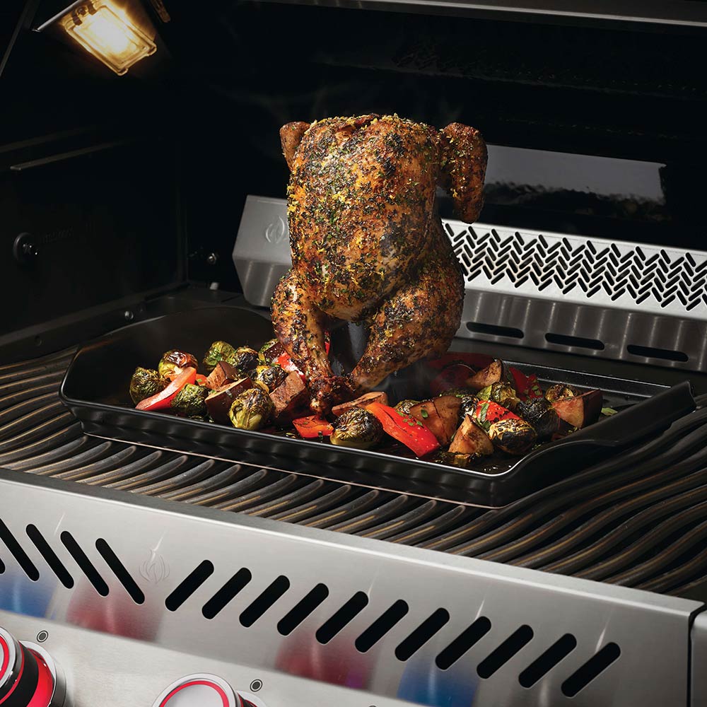 Roaster tray with upright beer-can holder holding roasted chicken on grill