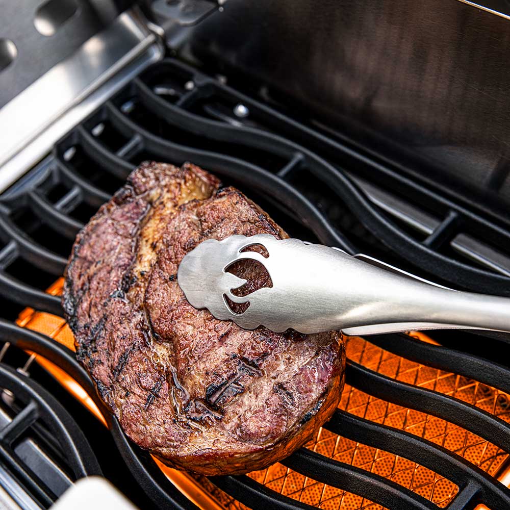 Side burner grill grates with cooked steak and metal tongs