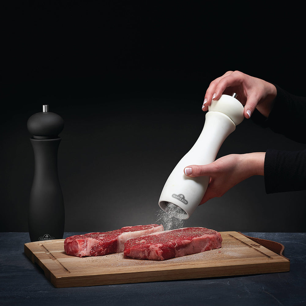 White salt grinder being turned over meat on a cutting board