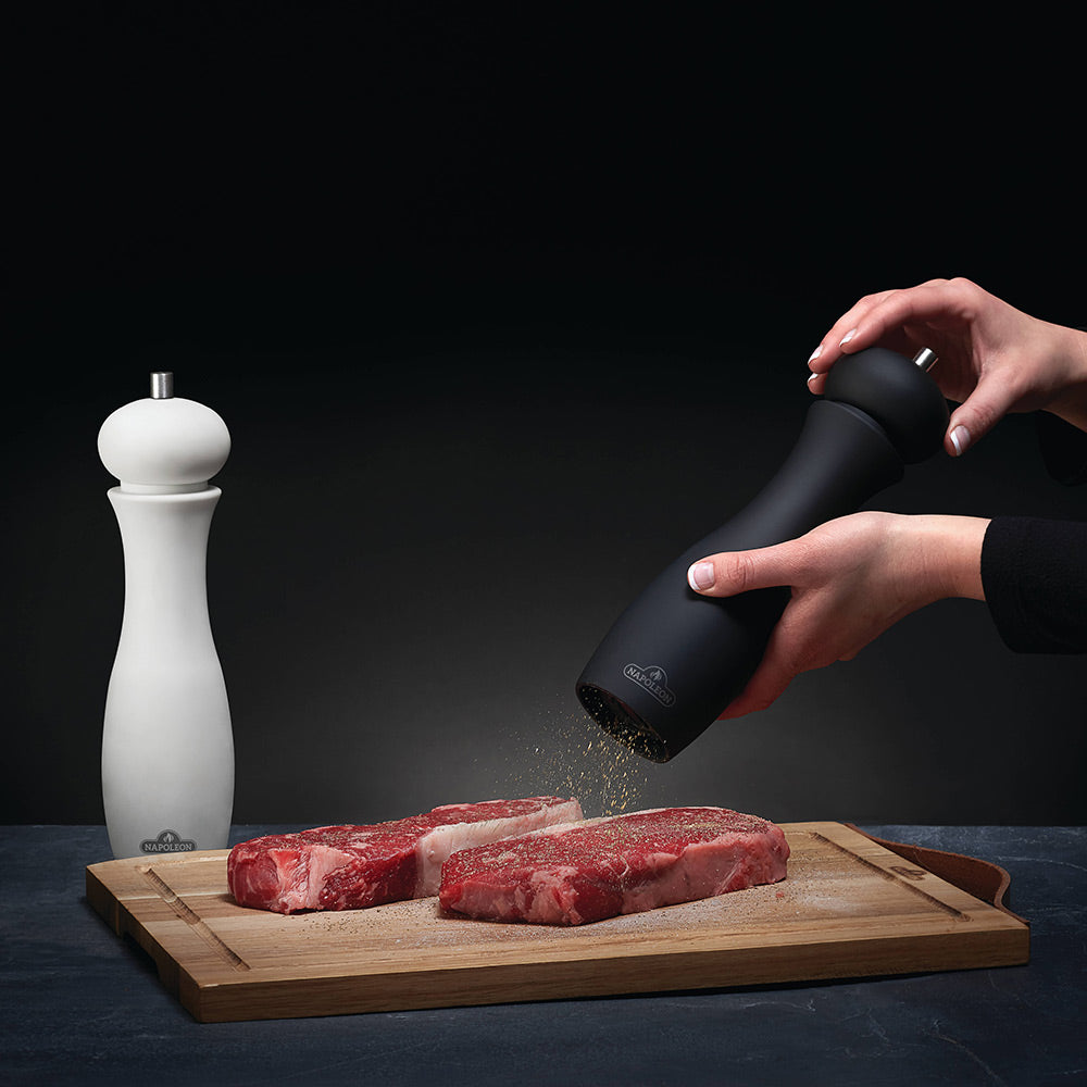 Black pepper grinder being turned over meat on a cutting board