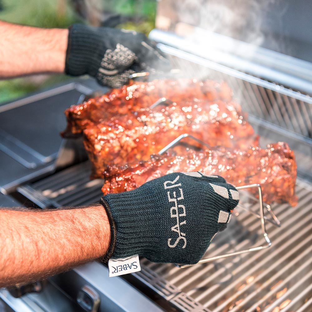 Person grilling ribs on a barbecue with 'Saber' branded gloves