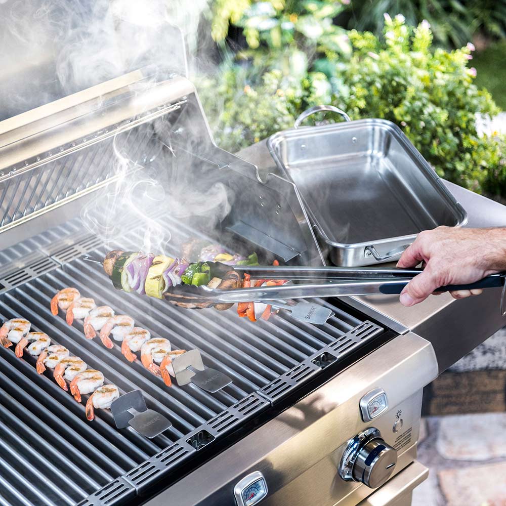 Stainless steel BBQ tongs grilling shrimp on a gas barbecue grate