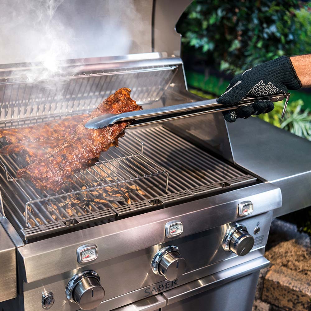 Stainless steel BBQ tongs lifting cooked meat on a barbecue grill