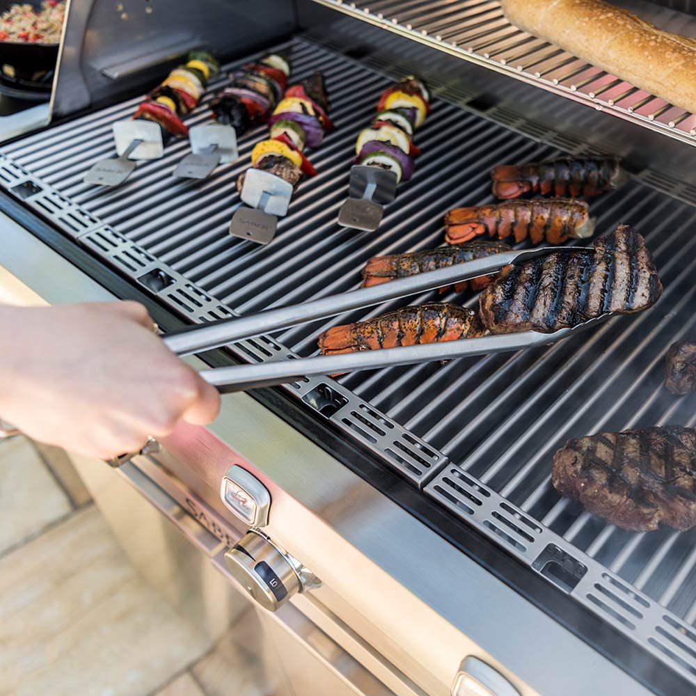 Stainless steel BBQ tongs turning fish on a barbecue grill grate
