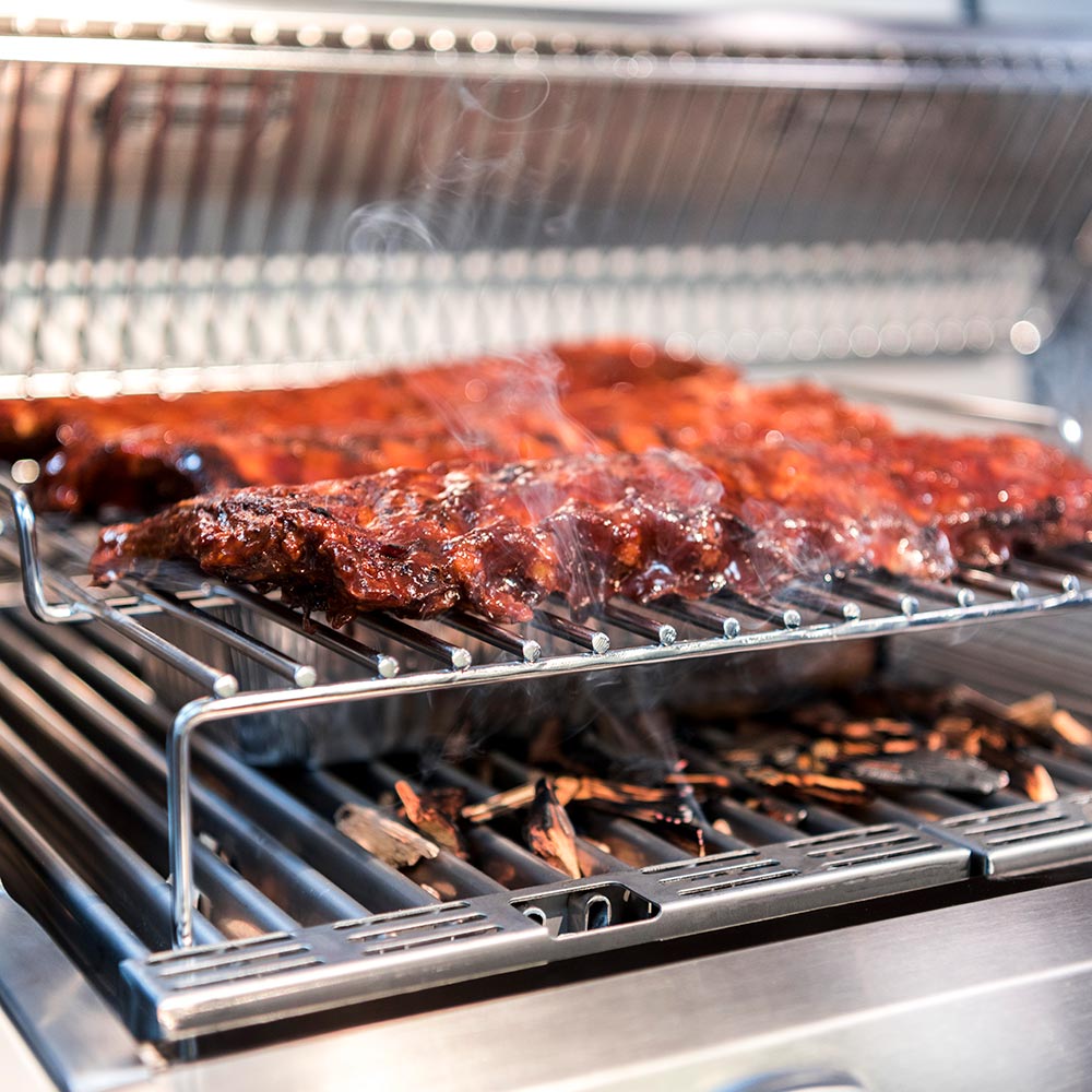 Roasting rack with browned meat on slotted wire bars over grill grates