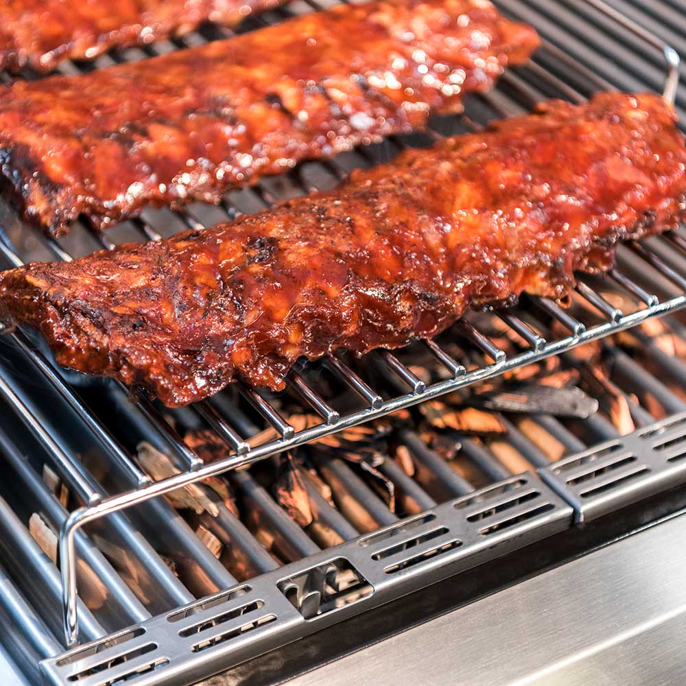 Roasting rack holding multiple browned meat pieces on wire bars above grill