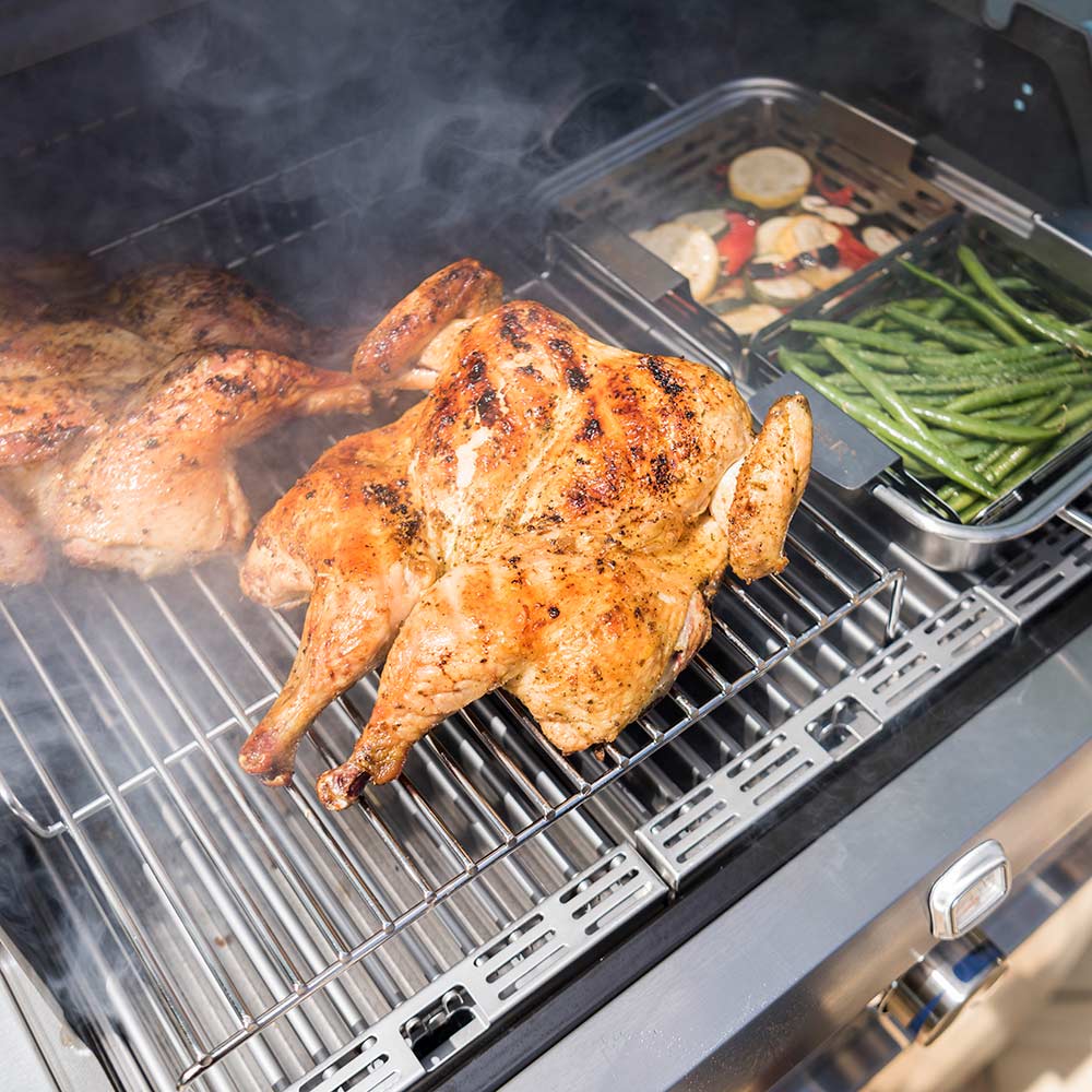 Angled view of grill with wire roasting rack holding chicken and vegetables