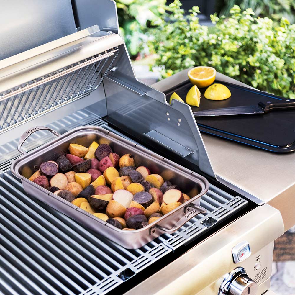 Roasting pan insert filled with mixed vegetables and lemon wedges on grill