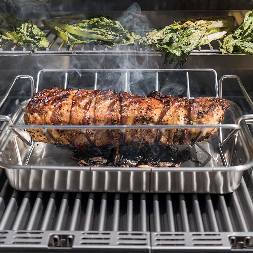 Roasting pan with browned meat log and smoke rising on grill