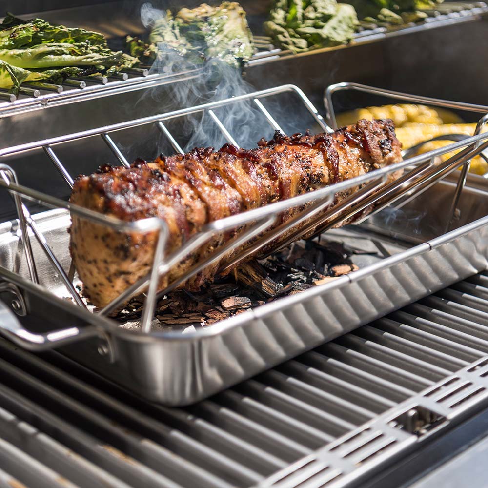 Roasting pan holding grilled meat with smoke, on an outdoor grill rack