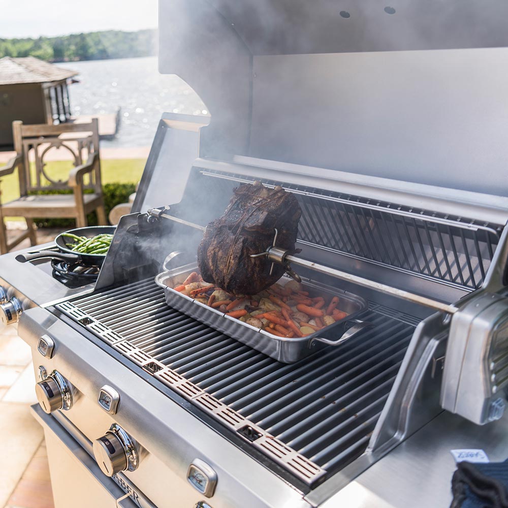 Roasting pan on grill with meat and vegetables, under cooking smoke