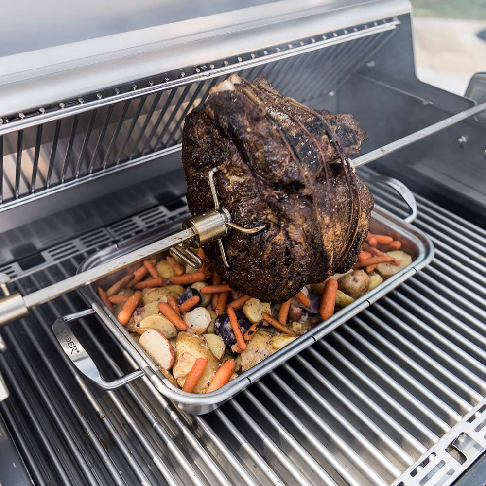 Roasting pan on grill with sliced carrots, potatoes, and a large cooked meat