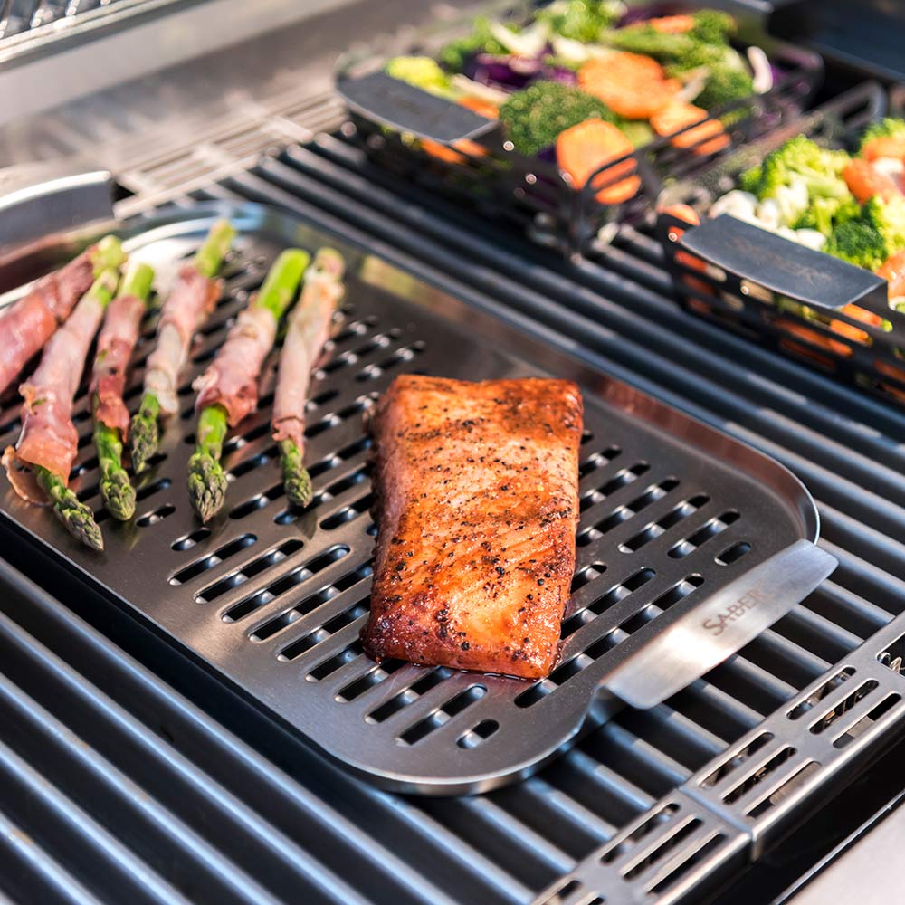 Stainless steel steamer tray on grill holding fish and asparagus