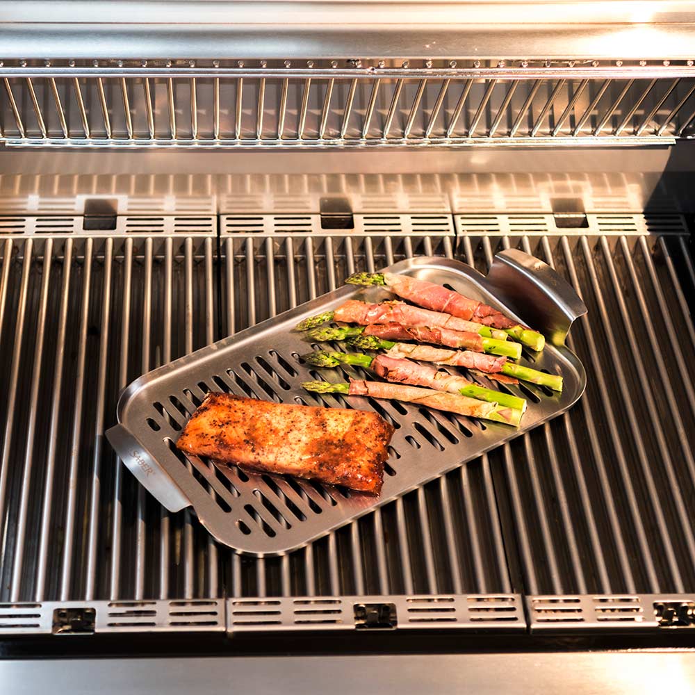 Stainless steel steamer tray holding fish and asparagus on grill grates