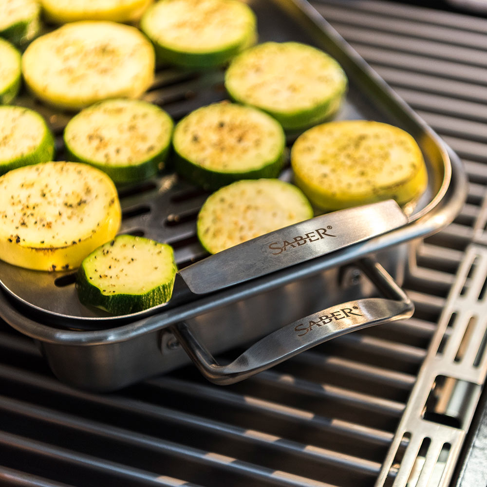 Stainless steel steamer tray with sliced zucchini rounds on grill grates