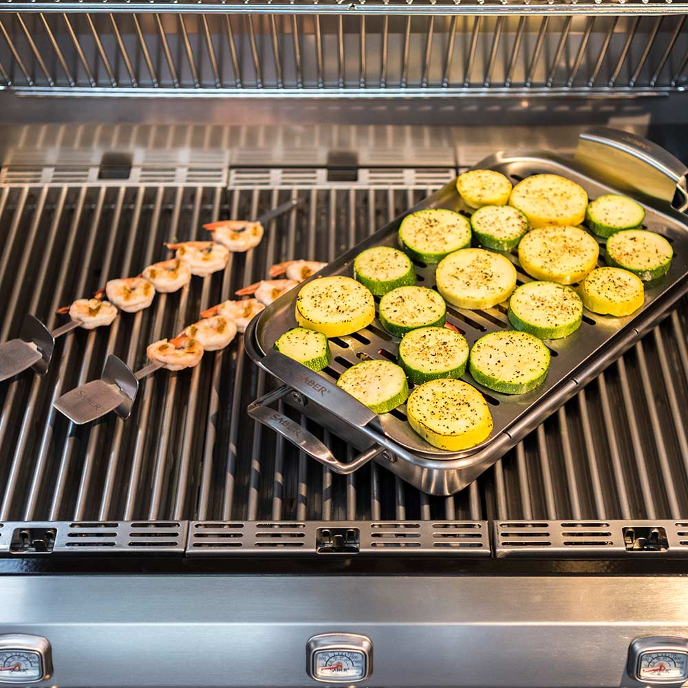 Stainless steel steamer tray with zucchini rounds and shrimp on grill grates