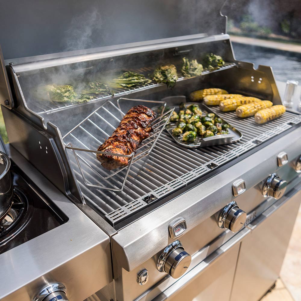 Stainless steel steamer tray with grilled meat and vegetables on a barbecue
