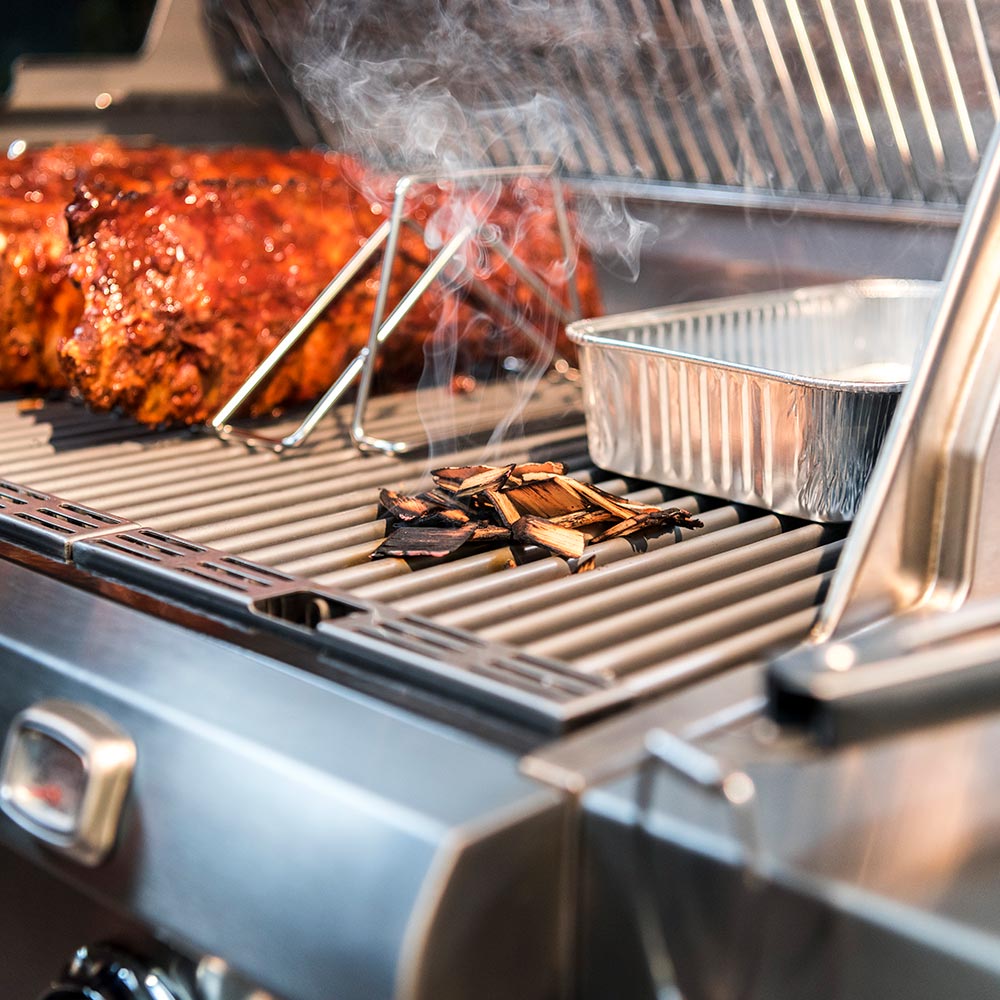 Stainless steel rib rack with grilled meat above grill grates and drifting smoke