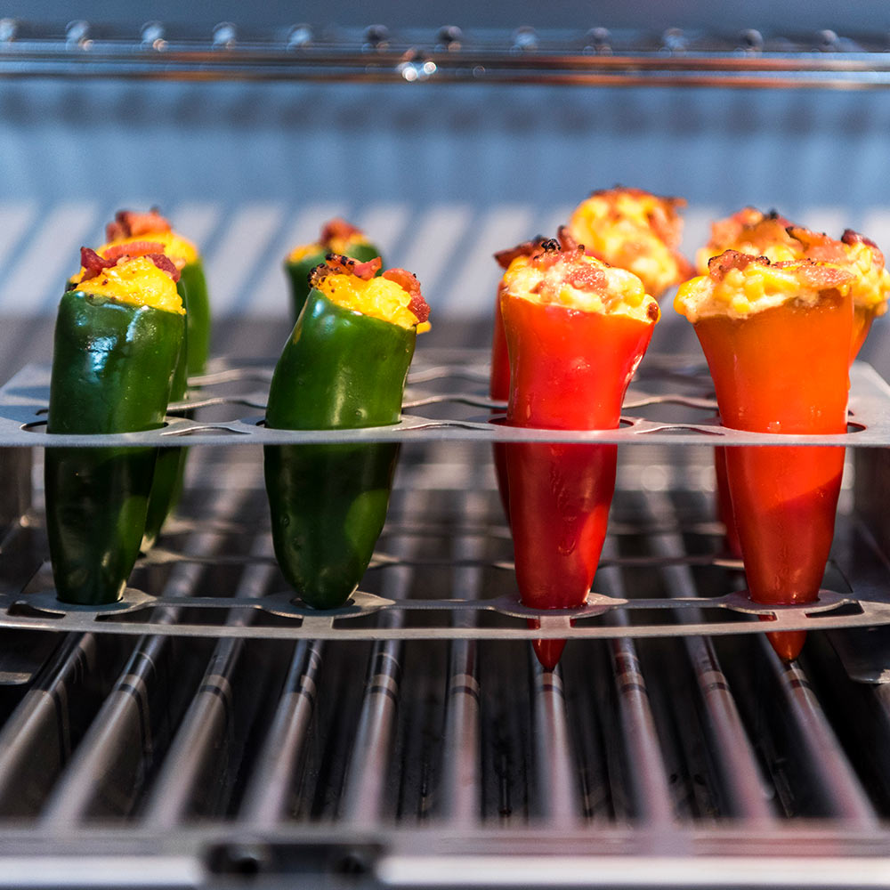 Double pepper roaster rack holding green and red stuffed peppers on a grill