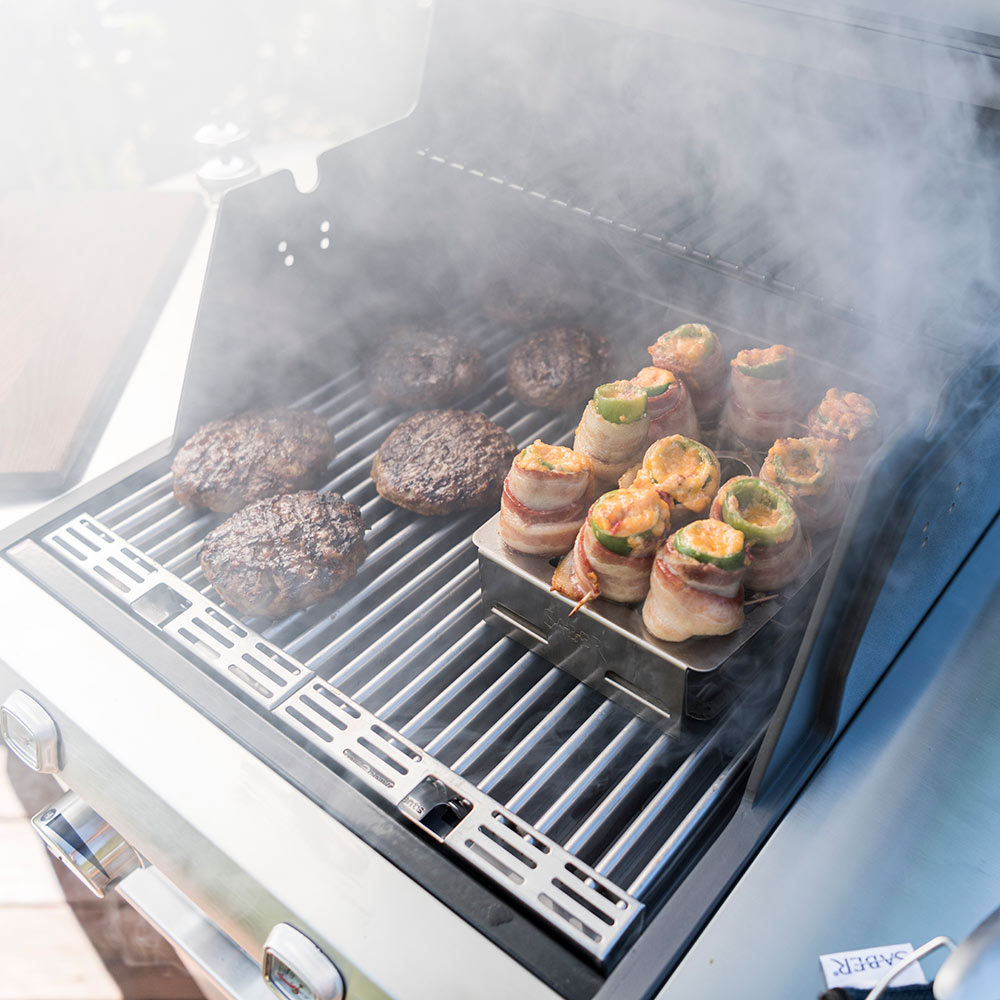 Stainless steel double pepper roaster with stuffed peppers, smoke rising on grill