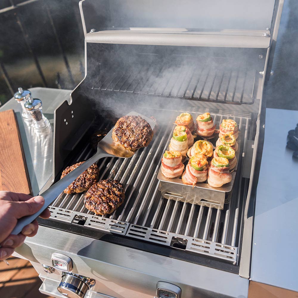 Stainless steel double pepper roaster on grill with peppers being placed by hand