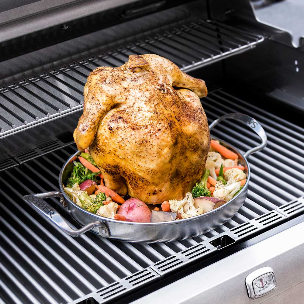 Stainless steel poultry roaster with handles holding roasted chicken and vegetables