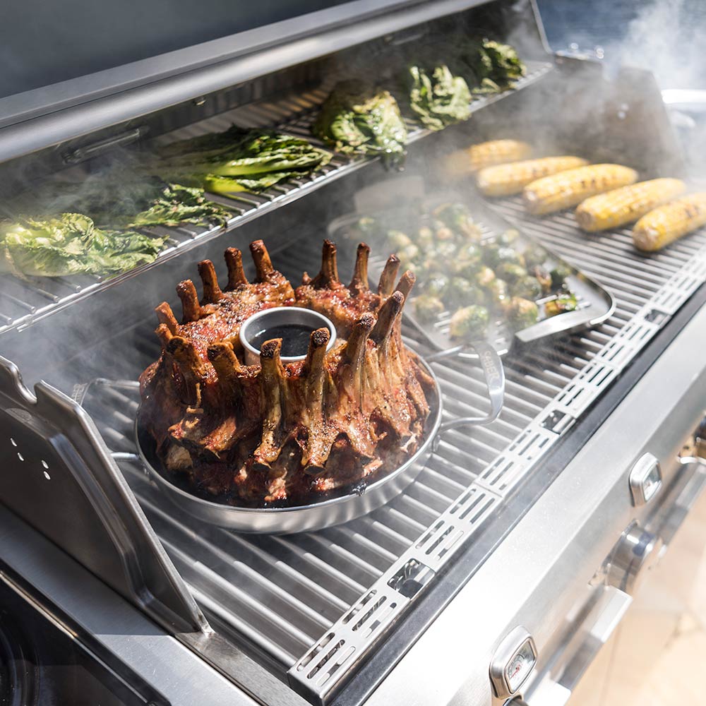 Stainless steel poultry roaster on grill grate, rack of meat with center cup