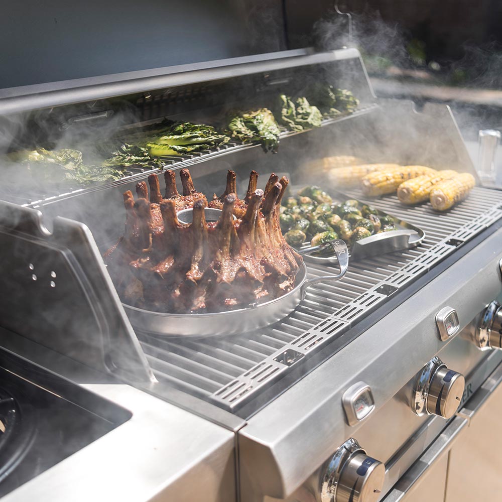 Stainless steel roaster on grill with rack meat, greens, and drifting smoke